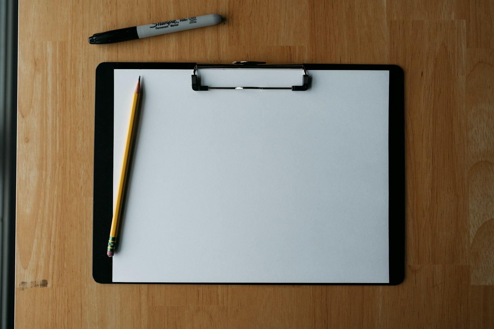 Clipboard, pencil, and pen on a wooden surface.